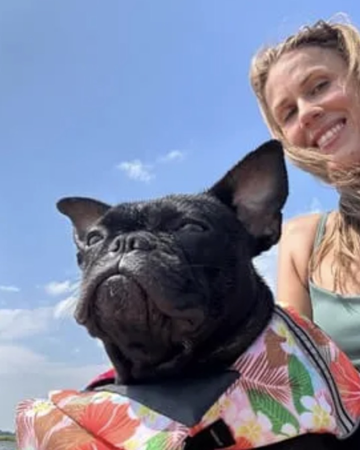 Owner and French bulldog in a floral life jacket by the water